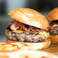 close-up of open faced buns and two bacon cheeseburgers